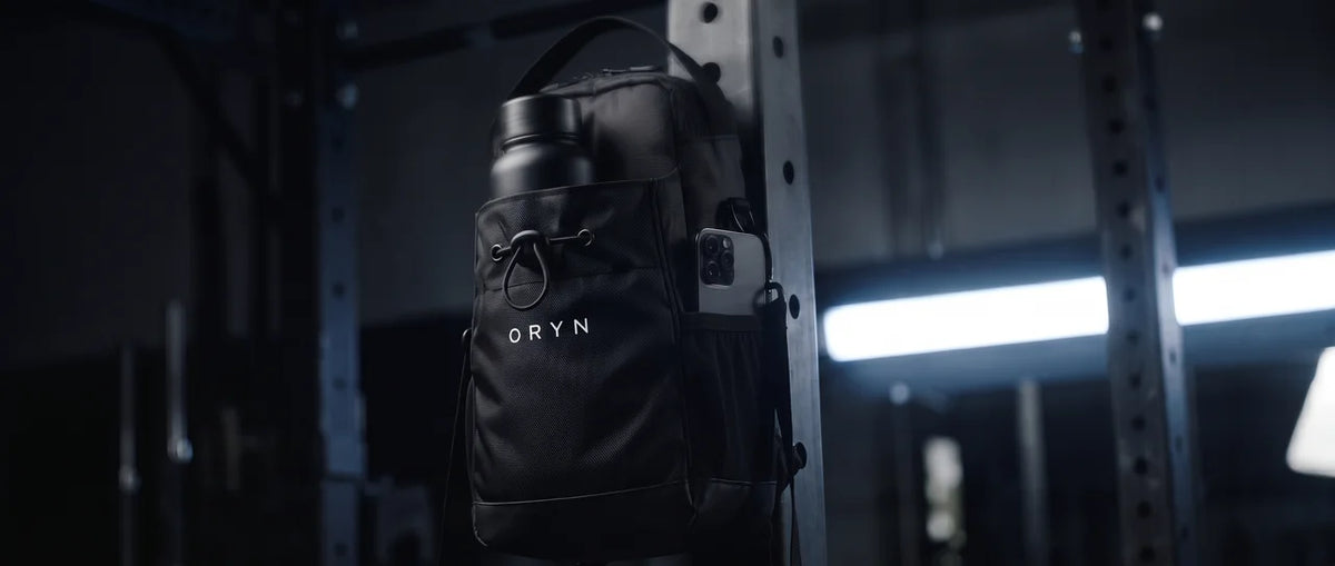 Sac Oryn accroché à un rack de musculation, gourde et téléphone dans les poches